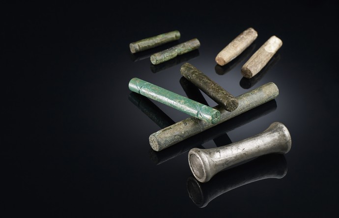 Mehrere kleine zylinderförmige Orakelstäbchen aus unterschiedlichen Materialien, darunter Knochen und Bronze.