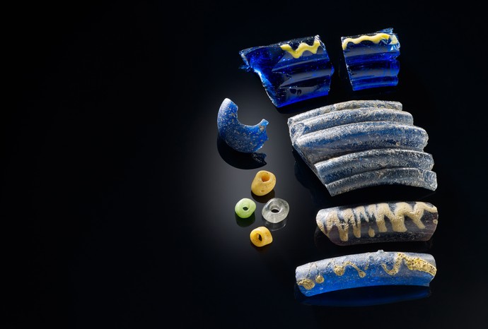 Mehrere Fragmente von Armringen aus blauem Glas, die mit einem gelbem Glasfaden verziert sind.