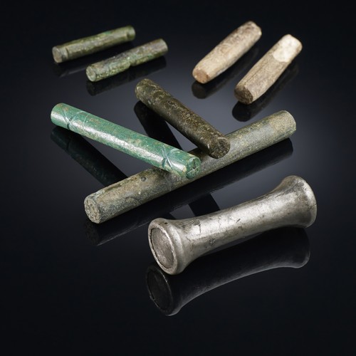 Mehrere kleine zylinderförmige Orakelstäbchen aus unterschiedlichen Materialien, darunter Knochen und Bronze.