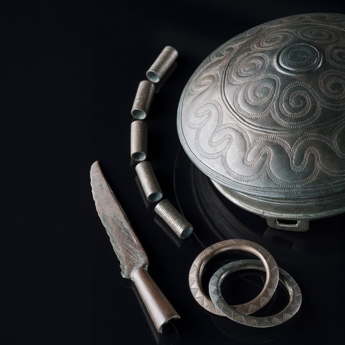 Mehrere Gegenstände aus grünlicher Bronze, darunter ein verziertes Becken und eine kleine Klinge.