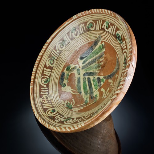 Bunt glasierte Keramikschüssel, die in der Mittel einen stilisierten Vogel zeigt.
