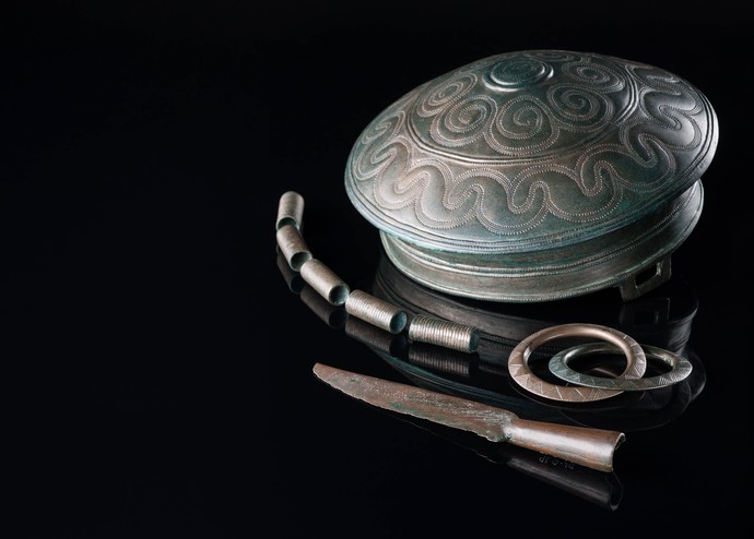 Mehrere Gegenstände aus grünlicher Bronze, darunter ein mit eingepunzten Wellenlinien und Kreisen verziertes Becken und eine kleine Klinge.