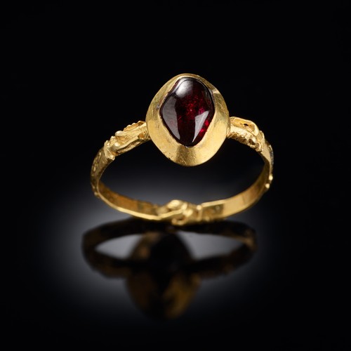 Goldener Ring mit einem Granat besetzt und mit Rautenmuster und an drei Stellen jeweils zwei sich umfassende Händen verziert.