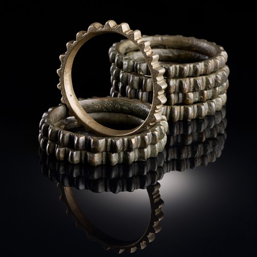 Mehrere Ringe aus goldfarbener Bronze, die mit Kerben versehen sind, sodass sie an Zahnräder erinnern.