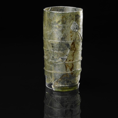 Zylinderförmiger Trinkbecher aus leicht grünlichem Glas mit mehreren horizontalen Markierungen.