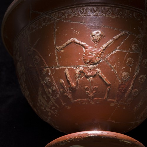 Nahaufnahme eines Trinkkelchs aus römischer Keramik, die ein tanzendes Skelett zeigt.