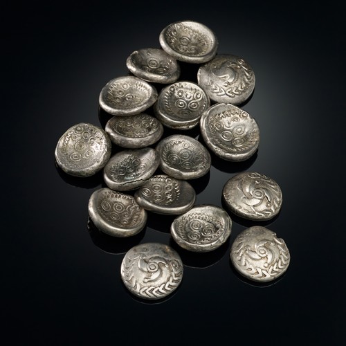 Mehrere kleine silberne Münzen, die gebogen sind und so die Form einer Schlüssel haben.