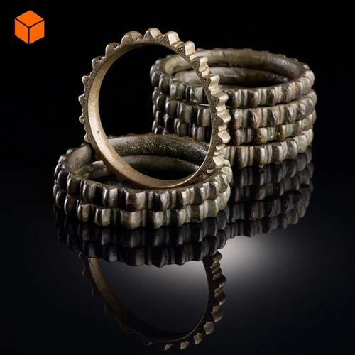 Mehrere Ringe aus goldfarbener Bronze, die mit Kerben versehen sind, sodass sie an Zahnräder erinnern.