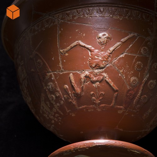 Nahaufnahme eines Trinkkelchs aus römischer Keramik, die ein tanzendes Skelett zeigt.