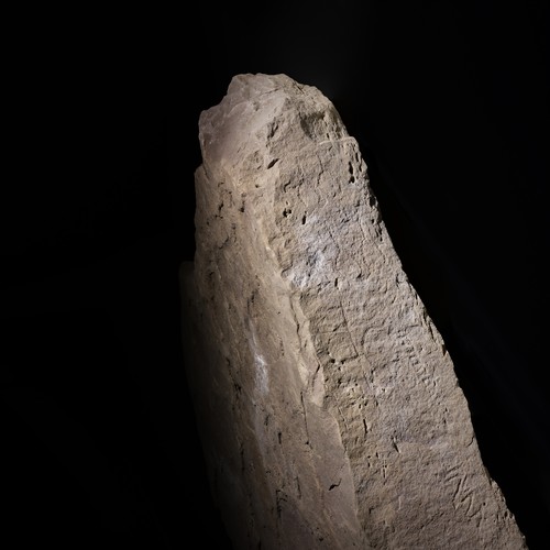 Große Steinplatte, auf deren Schmalseite eingeritzte Zeichen schwach zu erkennen sind.